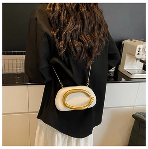 Close-up of white leather crossbody bag featuring a large gold C-shaped metal handle