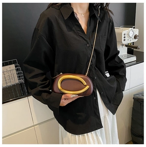 Detail of dark brown leather crossbody bag with elegant gold C-shaped metal ornament