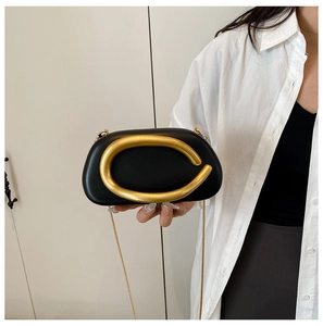 Detail of black leather shell bag with oversized matte gold C-shaped metal clasp and chain