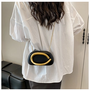 Detail of black semi-circle crossbody bag with large gold ring and chain on white shirt