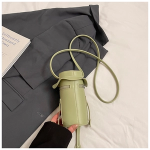 Top view of a pale green cylindrical crossbody bag with dual zippers on a fabric backdrop