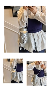 Detail of silver cylindrical crossbody bag featuring a cartoon character design with tiny legs
