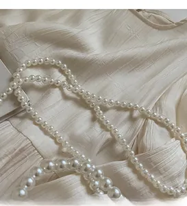 Detailed close-up of a long cream pearl crossbody strap on textured fabric