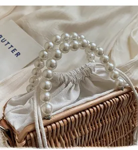 Detail of woven straw beach bag with glossy white faux pearl handles and drawstring inner pouch