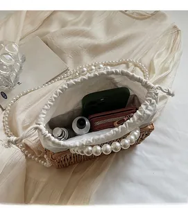 Detailed top view of a woven straw bag featuring pearl handles and a drawstring inner pouch