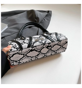 Detail of snake print cylindrical handbag with round handles and metallic accents