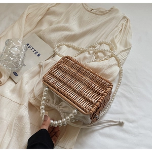 Detail of woven straw bag with faux pearl handles and drawstring liner on a beige dress