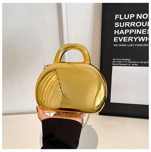 Detail of glossy metallic golden shell bag with integrated handle and thin chain strap