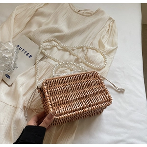 Close-up of woven straw basket bag with pearl handles and drawstring inner pouch