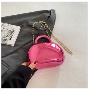 Detailed shot of metallic pink shell bag with golden chain strap held by hand