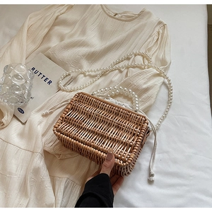 Detailed macro view of woven straw beach bag featuring dual pearl handles and canvas liner
