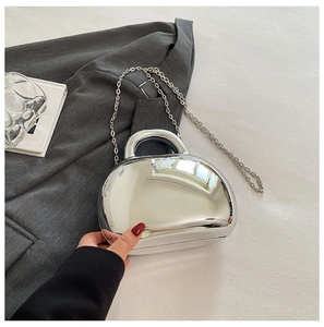 Detail of silver mirror acrylic shell bag with metallic handle and slim chain strap
