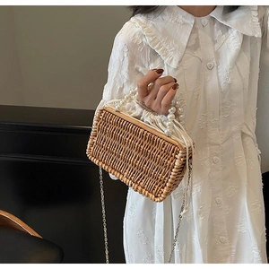 Detail of woven straw handbag featuring pearl top handle and gold chain shoulder strap