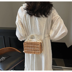 Detail of hand-woven straw bag with faux pearl ring handles and white drawstring liner