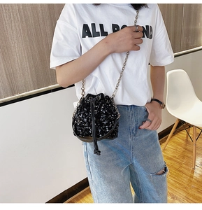 Chic black sequin drawstring bucket bag with silver chain strap worn by a female model