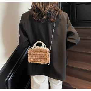 Detail of woven straw handbag featuring pearl top handle and silver chain strap