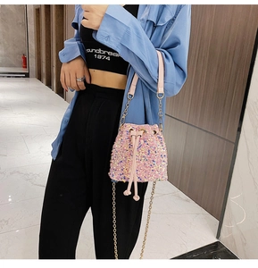 Pink sequined bucket bag with a chain strap and drawstring closure worn by a model