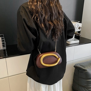 Brown shell-shaped crossbody bag with a gold C buckle and chain strap, worn by a model
