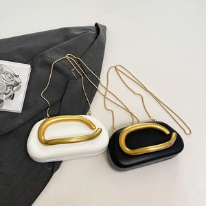 Minimalist shell-shaped crossbody bag with bold gold metal handle and chain strap