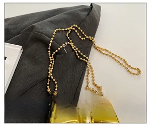 Detailed close-up of golden metal bead chain strap and metallic bow design on mini bag