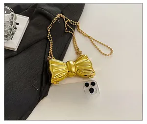 Detailed view of mini gold bow-shaped metal bag featuring a glossy finish and pearl chain
