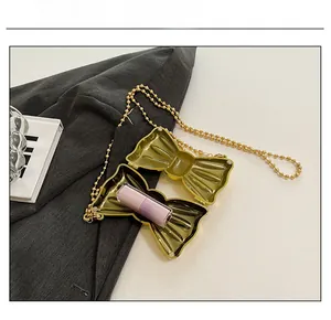 Detail view of mini gold bow clutch open with a lipstick inside on grey suit fabric