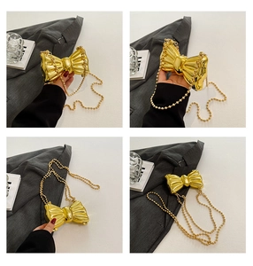 Detail of a shiny gold bow-shaped mini bag with a delicate metal bead chain strap