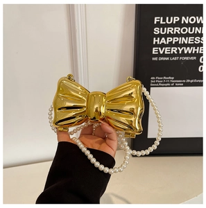 Detailed view of golden metal bow evening bag with elegant pearl chain strap and mirror finish