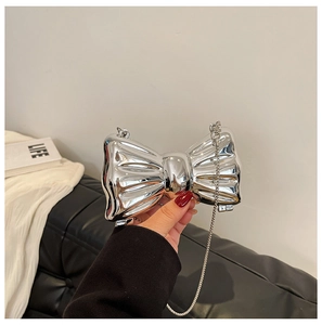 Close-up of a metallic silver bow-shaped mini bag with a fine chain strap being held