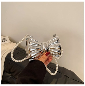 Detail of silver metallic bow-shaped handbag with elegant pearl chain strap in hand