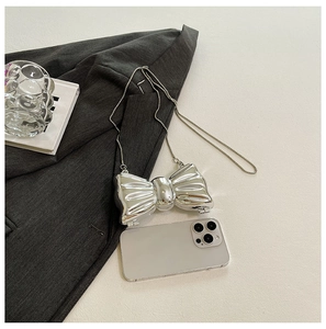 Silver bow-shaped mini crossbody bag shown with a smartphone for size reference