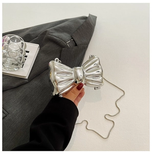 Detail of silver metallic bow bag with shiny finish and delicate chain strap