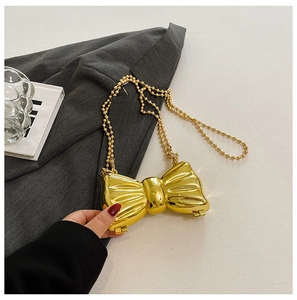 Detailed macro of the metallic bow handbag showing the gold finish and pearl chain