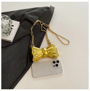 Detailed top view of gold metallic bow mini bag with pearl chain next to a smartphone