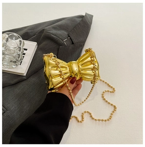 Detailed close-up of a metallic gold bow-shaped clutch with a pearl bead chain strap