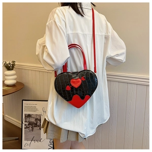 Detail of heart-shaped handbag in black croc leather with red arrow and wavy trim