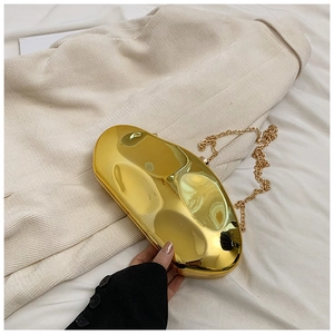 Macro shot of glossy gold metallic evening clutch bag with chain strap held by hand