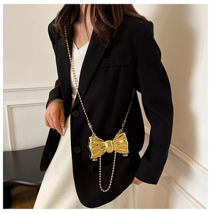 Close-up of metallic bow bag with pearl chain shown on model in modern outfit