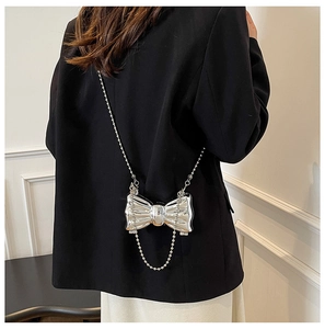 Close-up of metallic silver bow mini bag with pearl chain on black blazer jacket