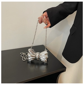 Close-up of metallic silver bow handbag featuring a polished finish and pearl chain link