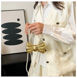 Detail of metallic gold bow-shaped mini bag with white pearl chain strap and glossy finish