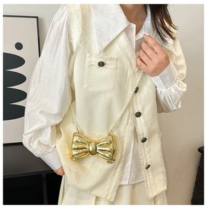 Detailed view of golden metallic bow bag with elegant white pearl crossbody chain