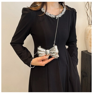 Detail of silver metallic bow-shaped mini bag with elegant pearl chain on a dress