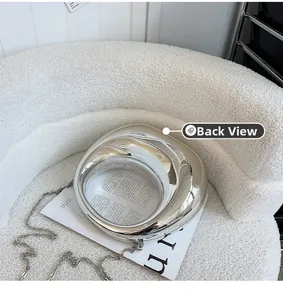 Sac à main croissant argenté miroir posé sur un canapé en bouclé blanc doux