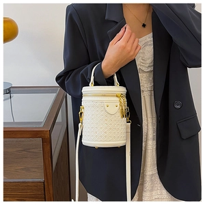 Detail of white cylindrical bucket bag with woven texture and gold ring handle accessory