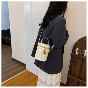 Detail of white cylindrical bucket bag with woven texture and gold-tone hardware on shoulder