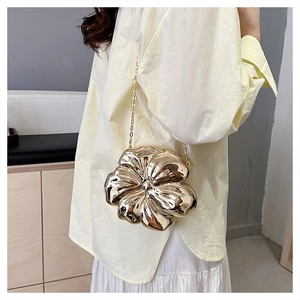 Detail of a luxury gold flower clutch bag with reflective metallic finish and chain