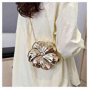 Close-up of golden flower-shaped hard shell clutch bag with delicate chain strap on model