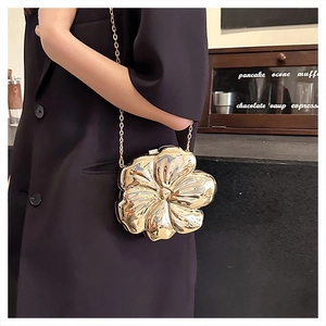 Chic gold metallic flower clutch bag with delicate chain strap worn by a model