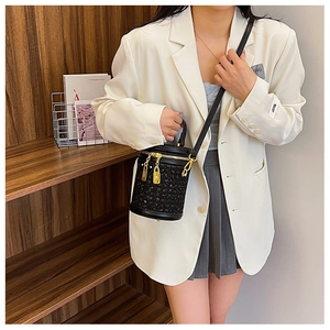 Detail view of a black rhinestone cylinder bag styled with a white blazer on a model